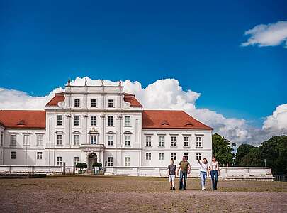 Ein Elternpaar mit zwei jugendlichen Kindern läuft vor dem Schloss Oranienburg.