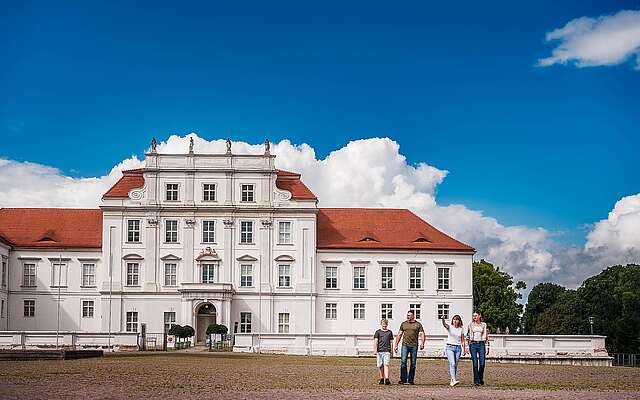 Ein Elternpaar mit zwei jugendlichen Kindern läuft vor dem Schloss Oranienburg.