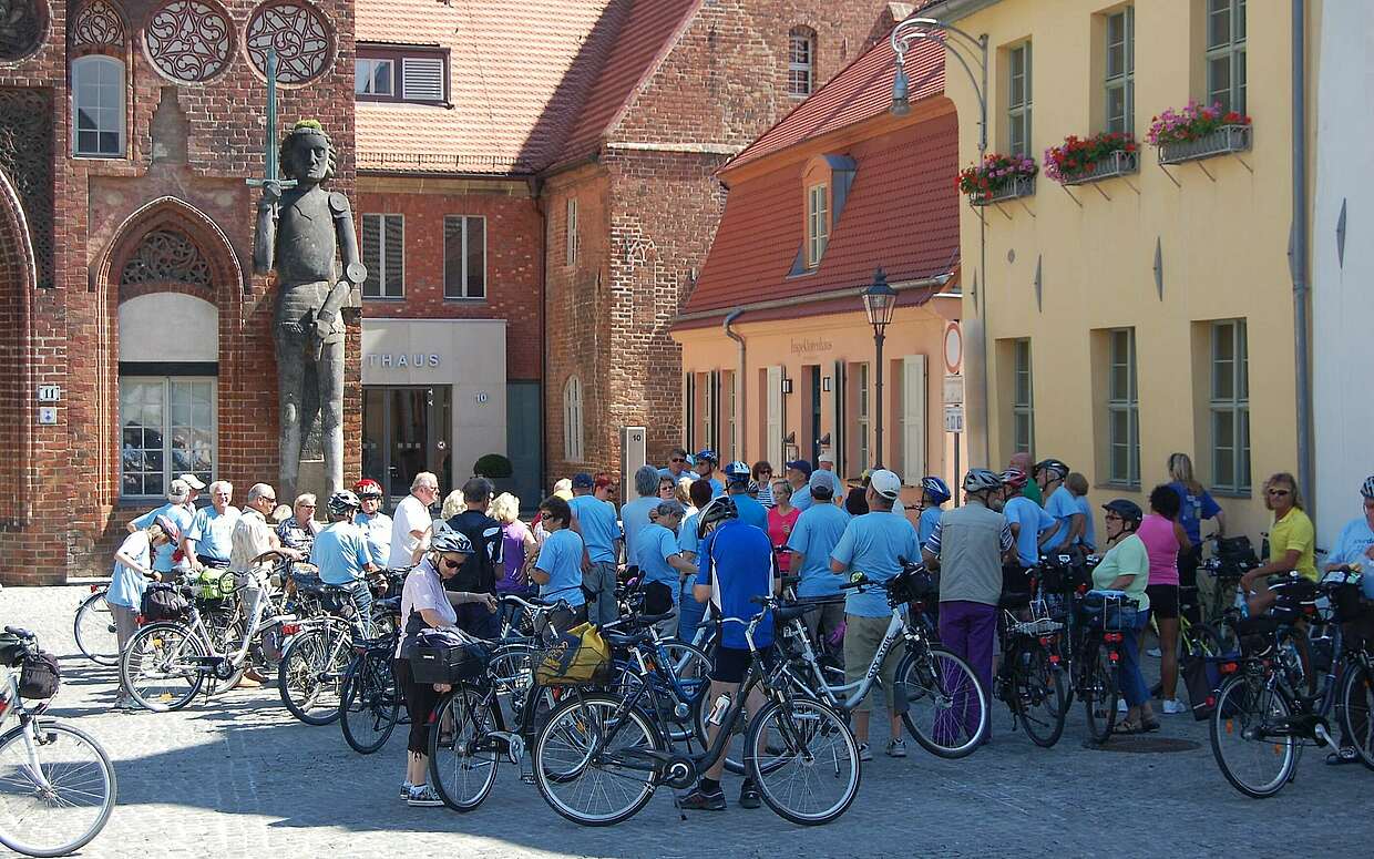Eine Radler-Gruppe besichtigt das Altstädtische Rathaus mit dem Roland davor.