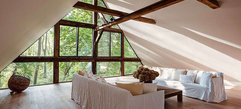 Wohnbereich mit weißen Sofas und Panoramafenster mit Waldblick