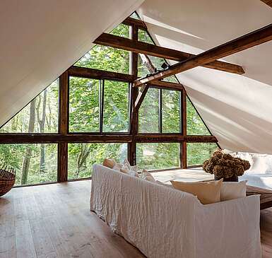Wohnbereich mit weißen Sofas und Panoramafenster mit Waldblick