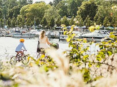 Frau und Kind fahren gemeinsam am Wasser entlang Rad