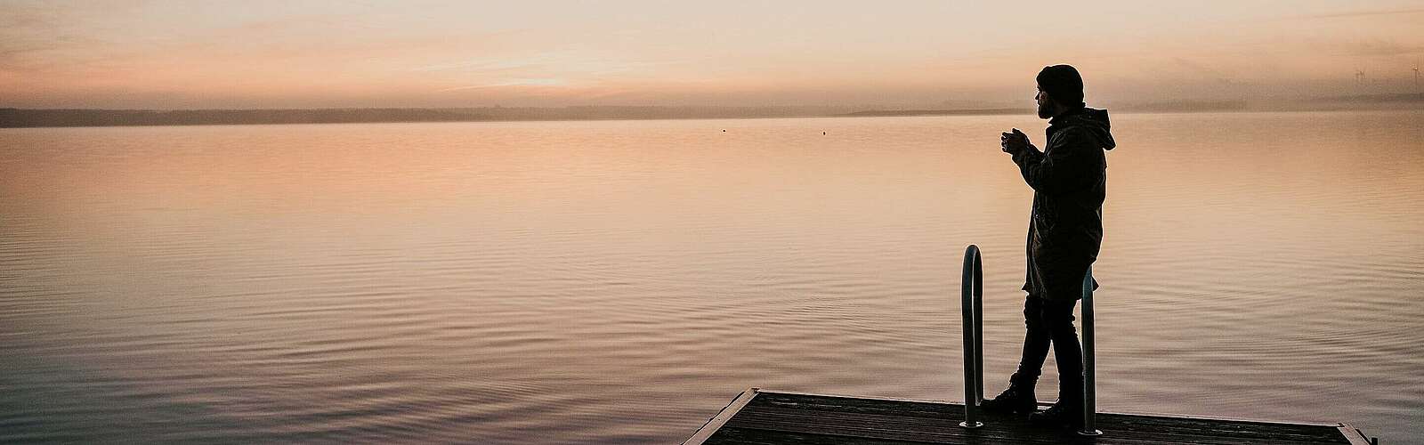 Mann auf einem Badesteg bei Sonnenaufgang