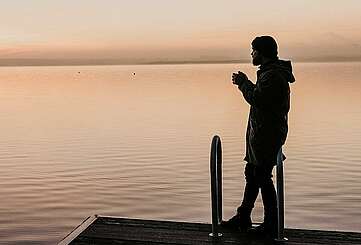 Mann auf einem Badesteg bei Sonnenaufgang