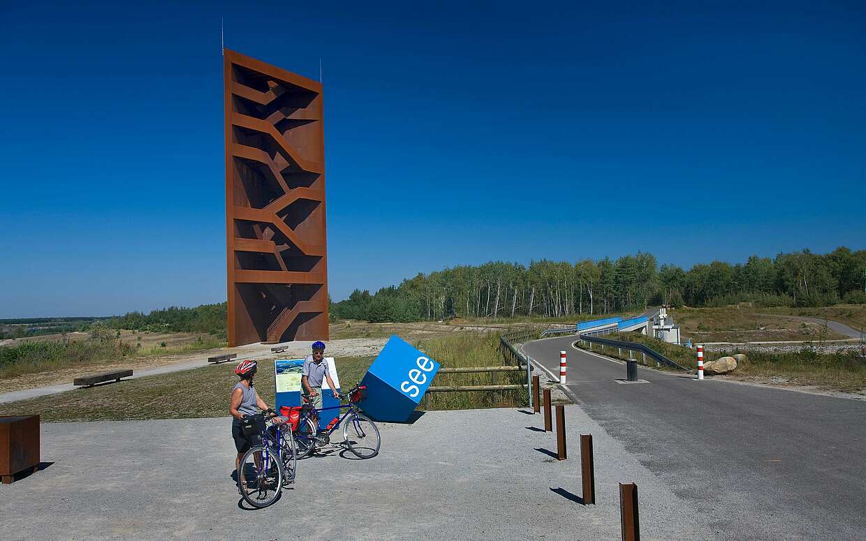 Radfahrer an der Landmarke Rostiger Nagel am Sedlitzer See